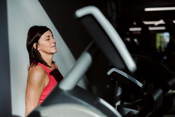 A content senior woman in gym resting after doing exercise, eyes closed. Copy space.