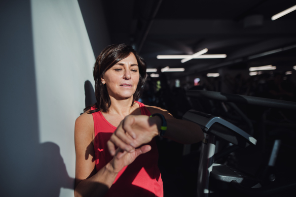 A content senior woman with smartwatch in gym resting after doing exercise, checking time. Copy space.