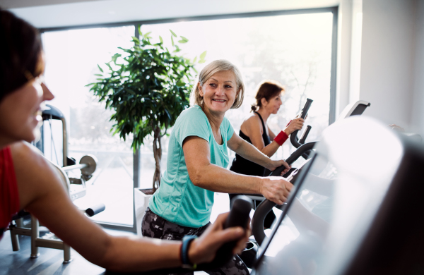 A group of seniors in gym with a young trainer doing cardio work out, exercising on stationary bicycle.