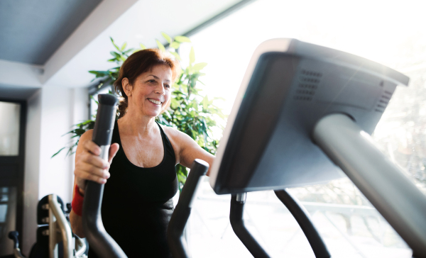 A cheerful female senior in gym doing cardio workout, exercising on stationary bicycle.