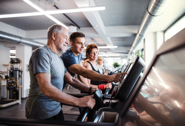 A group of seniors in gym with a young trainer doing cardio work out, exercising on stationary bicycle.