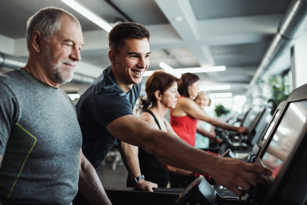 A group of seniors in gym with a young trainer doing cardio work out, exercising on stationary bicycle.