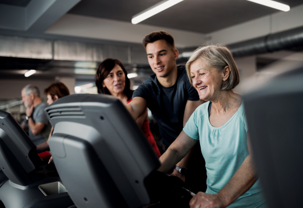 A group of seniors in gym with a young trainer doing cardio work out, exercising on stationary bicycle.