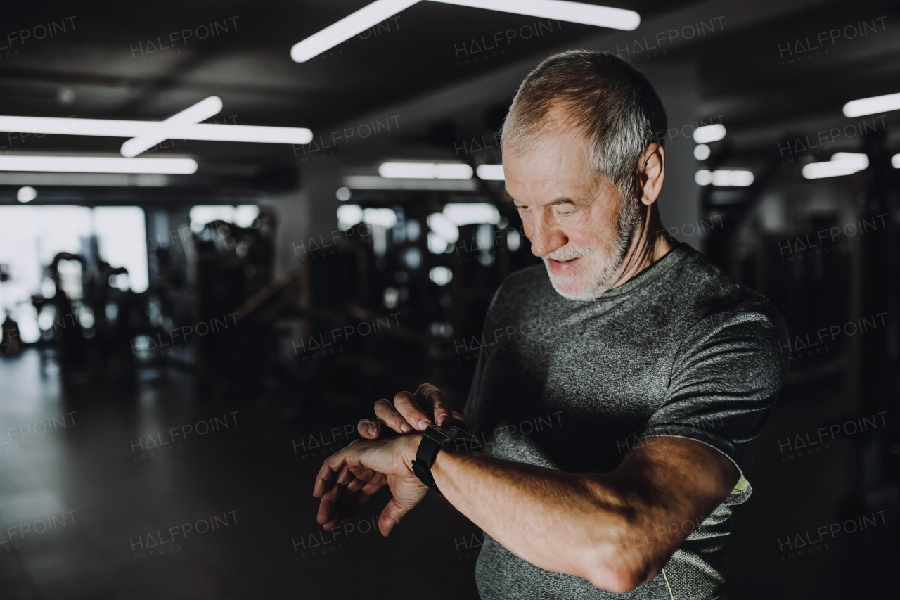 A cheerful senior man with smartwatch in gym measuring time while doing exercise. Copy space.