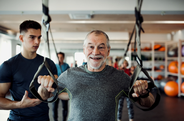 A group of cheerful seniors in gym with a young personal trainer doing exercise with TRX.