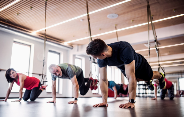 A group of cheerful seniors in gym with a young personal trainer doing exercise with TRX.