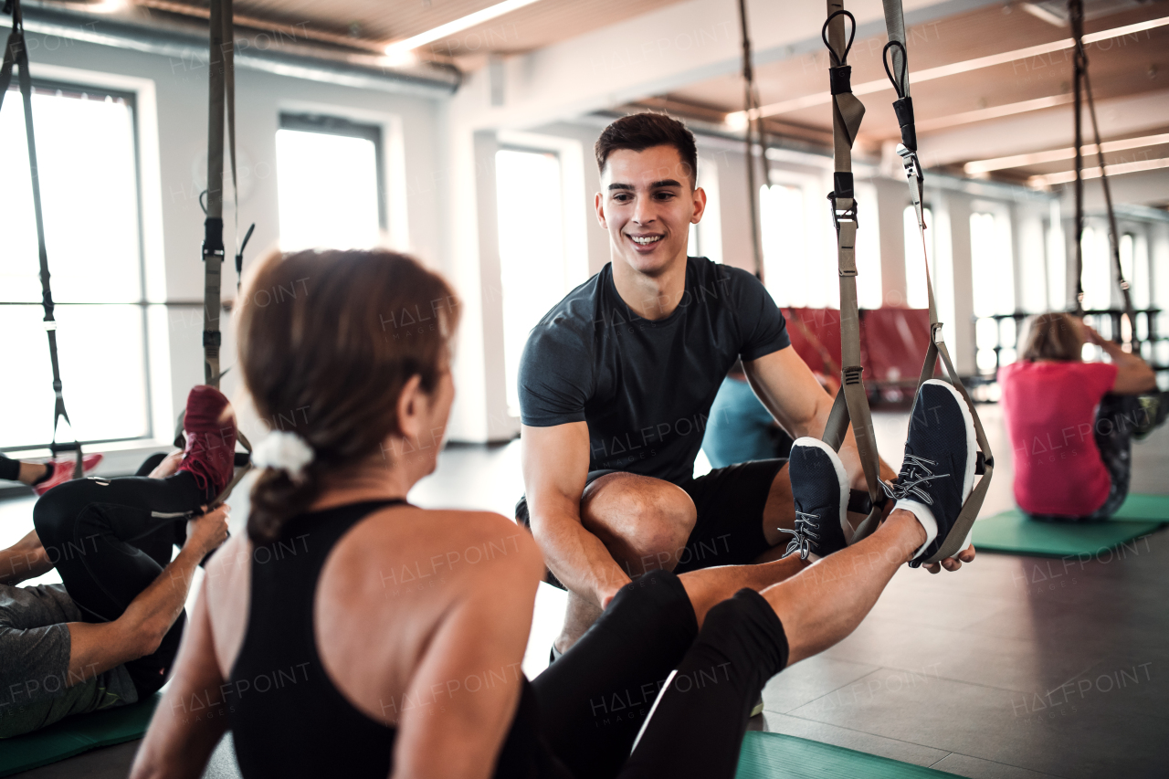 A group of cheerful seniors in gym with a young personal trainer doing exercise with TRX.