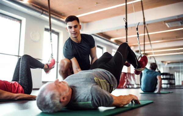 A group of cheerful seniors in gym with a young personal trainer doing exercise with TRX.