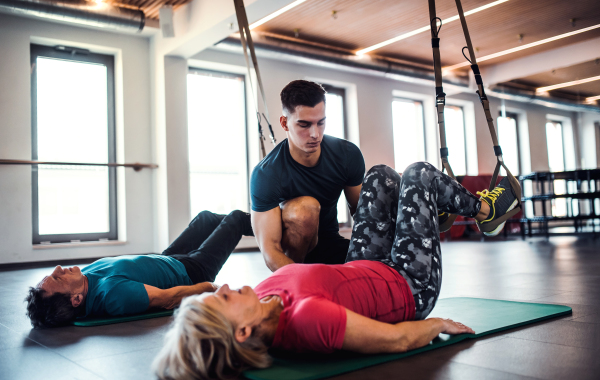 A group of cheerful seniors in gym with a young personal trainer doing exercise with TRX.