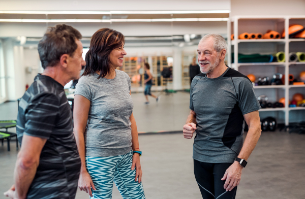 A group of cheerful seniors in gym resting after doing exercise, standing and talking.