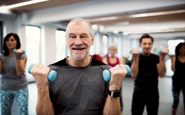 A group of cheerful seniors standing in gym doing exercise with dumbbells.