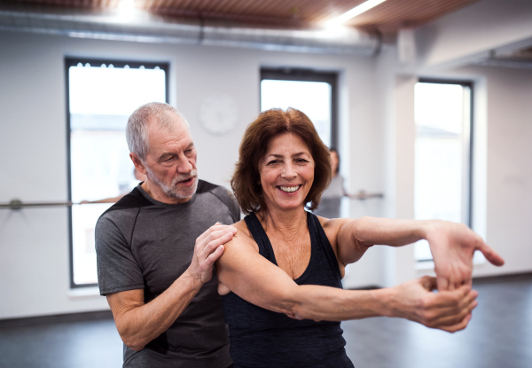 A cheerful senior woman in gym doing exercise with a personal trainer.