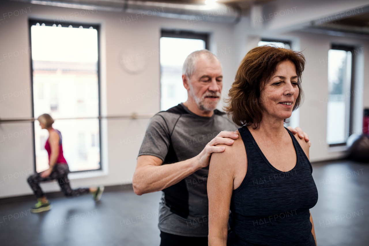 A cheerful senior woman in gym doing exercise with a personal trainer.