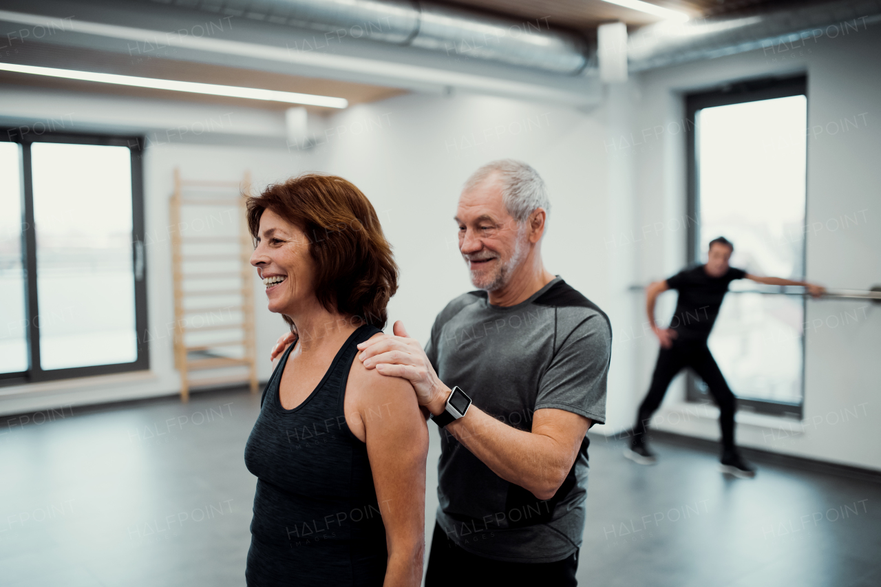 A cheerful senior woman in gym doing exercise with a personal trainer.