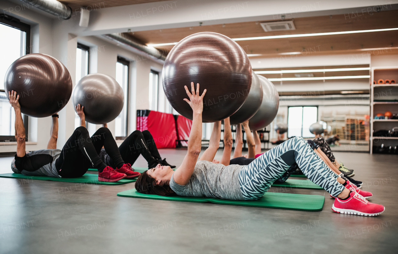 A group of cheerful seniors in gym doing exercise with fit balls, lifting them.