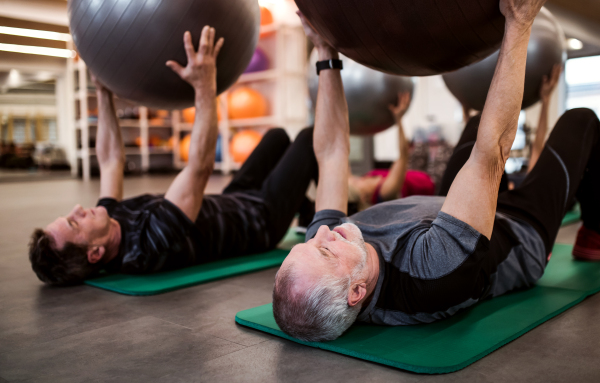 A group of cheerful seniors in gym doing exercise with fit balls, lifting them.