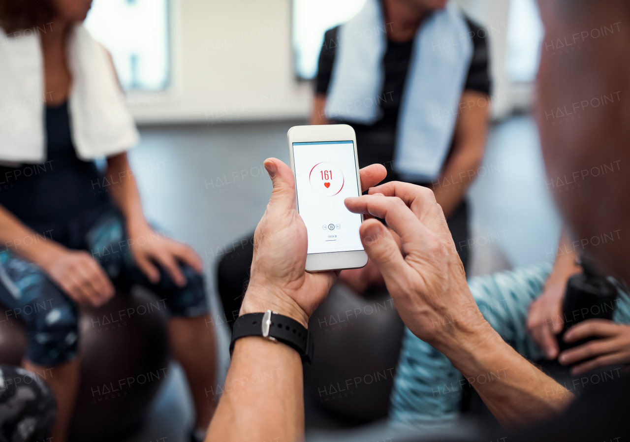 A midsection of group of seniors with smartphone in gym checking heart rate and resting after doing exercise.