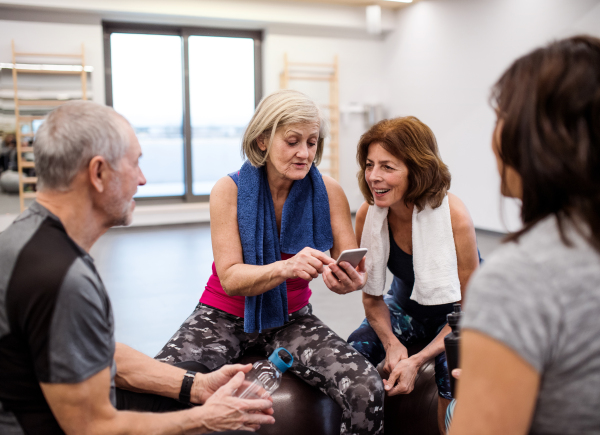 A group of seniors with smartphone in gym resting after doing exercise on fit balls.