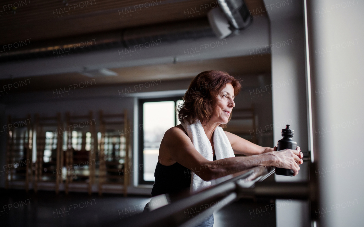 A content senior woman with water bottle in gym resting after doing exercise. Copy space.