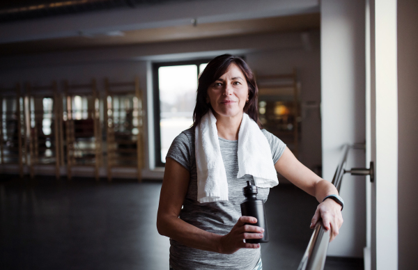 A content senior woman with water bottle in gym resting after doing exercise. Copy space.