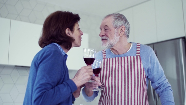 A portrait of happy senior couple in kitchen indoors at home, clinking glasses.