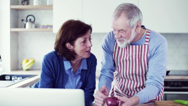 A portrait of happy senior couple with laptop indoors at home, cooking.