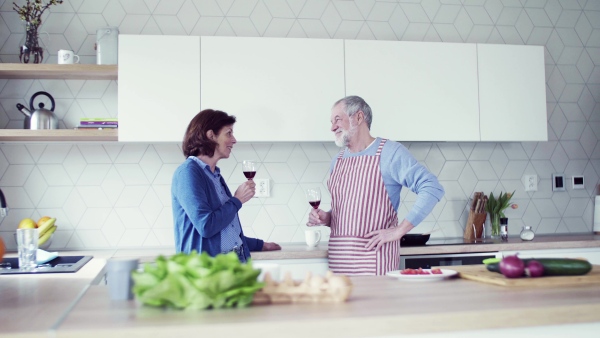 A portrait of happy senior couple in kitchen indoors at home, clinking glasses.