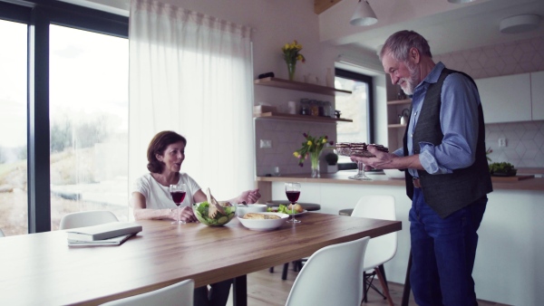 A senior couple in love having lunch indoors at home, talking.