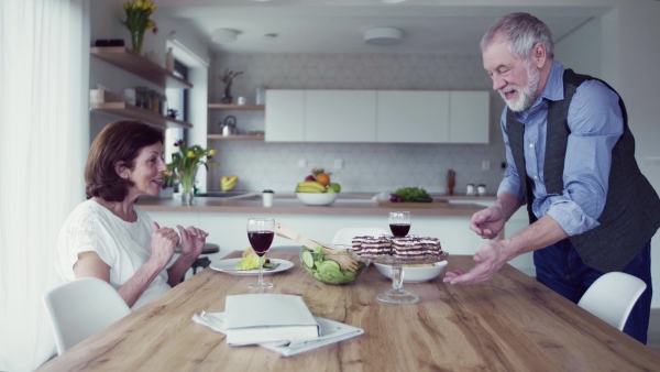 A senior couple in love having lunch indoors at home, talking.