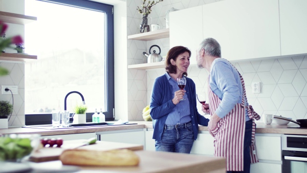 A portrait of happy senior couple in kitchen indoors at home, clinking glasses.