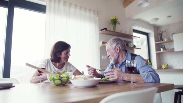 A senior couple in love having lunch indoors at home, talking.