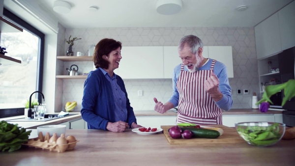 A portrait of happy senior couple in love indoors at home, preparing food. Slow motion.