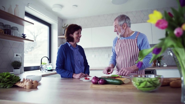 A portrait of happy senior couple in love indoors at home, preparing food. Slow motion.