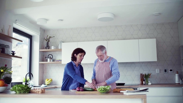 A portrait of happy senior couple in love indoors at home, preparing food. Slow motion.