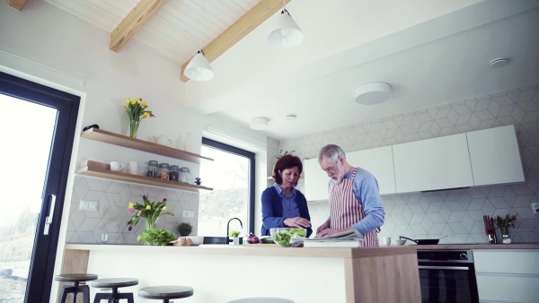 A portrait of happy senior couple in love indoors at home, preparing food. Slow motion.