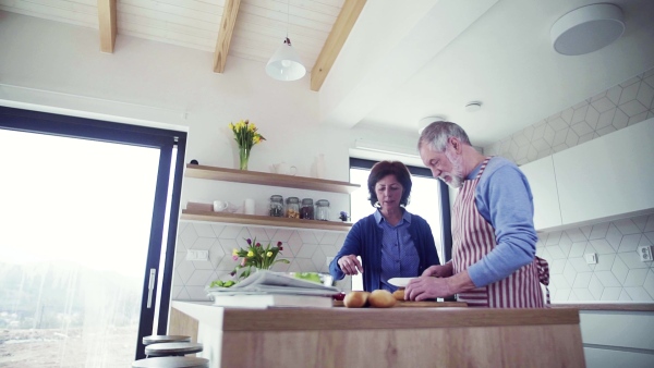 A portrait of happy senior couple in love indoors at home, preparing food. Slow motion.