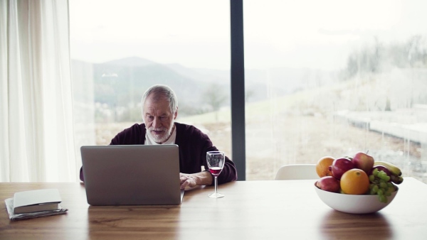 A portrait of senior man indoors at home, using laptop. Slow motion.