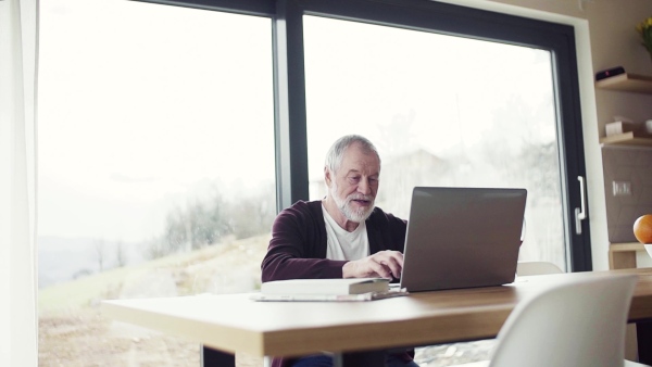 A portrait of senior man indoors at home, using laptop. Slow motion.