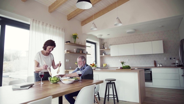 A senior couple in love having lunch indoors at home, serving. Slow motion.