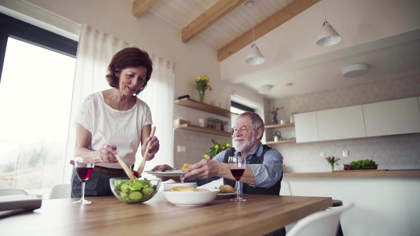 A senior couple in love serving lunch indoors at home, talking. Slow motion.