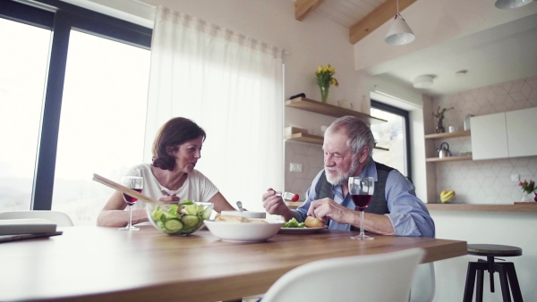 A senior couple in love having lunch indoors at home, talking. Slow motion.