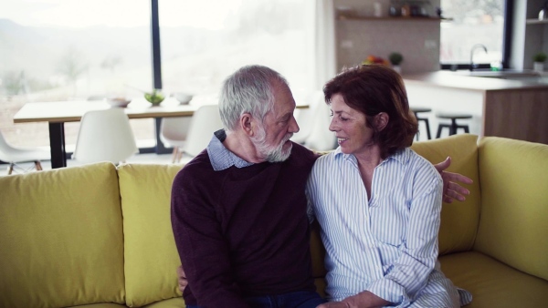 An affectionate senior couple in love sitting on sofa indoors at home, talking. Slow motion.