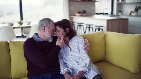 An affectionate senior couple in love sitting on sofa indoors at home, talking. Slow motion.