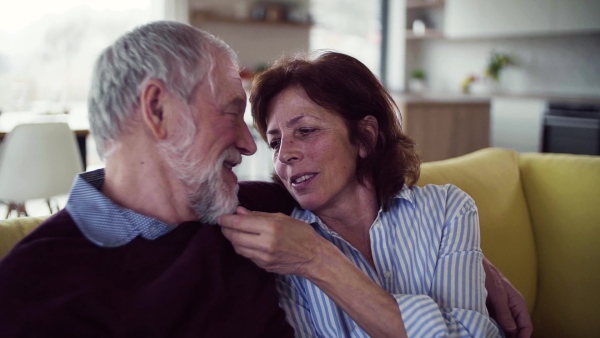 An affectionate senior couple in love sitting on sofa indoors at home, talking. Slow motion.