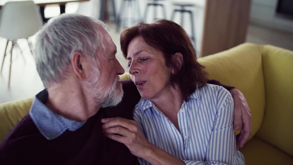 An affectionate senior couple in love sitting on sofa indoors at home, talking. Slow motion.