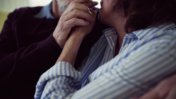 An affectionate senior couple in love sitting on sofa indoors at home, talking and kissing. Slow motion.