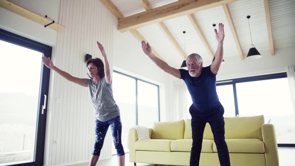 A happy senior couple indoors at home, doing exercise indoors. Slow motion.