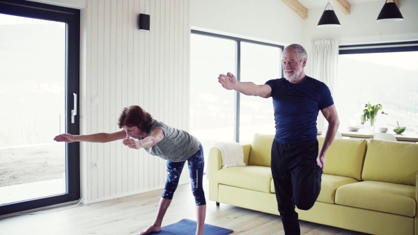 A happy senior couple indoors at home, doing exercise indoors. Slow motion.