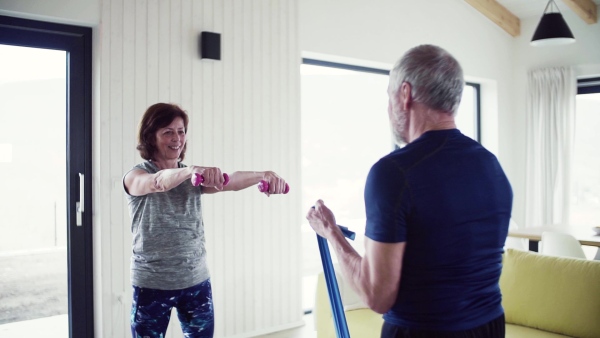 A happy senior couple indoors at home, doing exercise indoors. Slow motion.