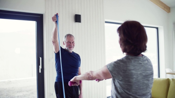 A happy senior couple indoors at home, doing exercise indoors. Slow motion.